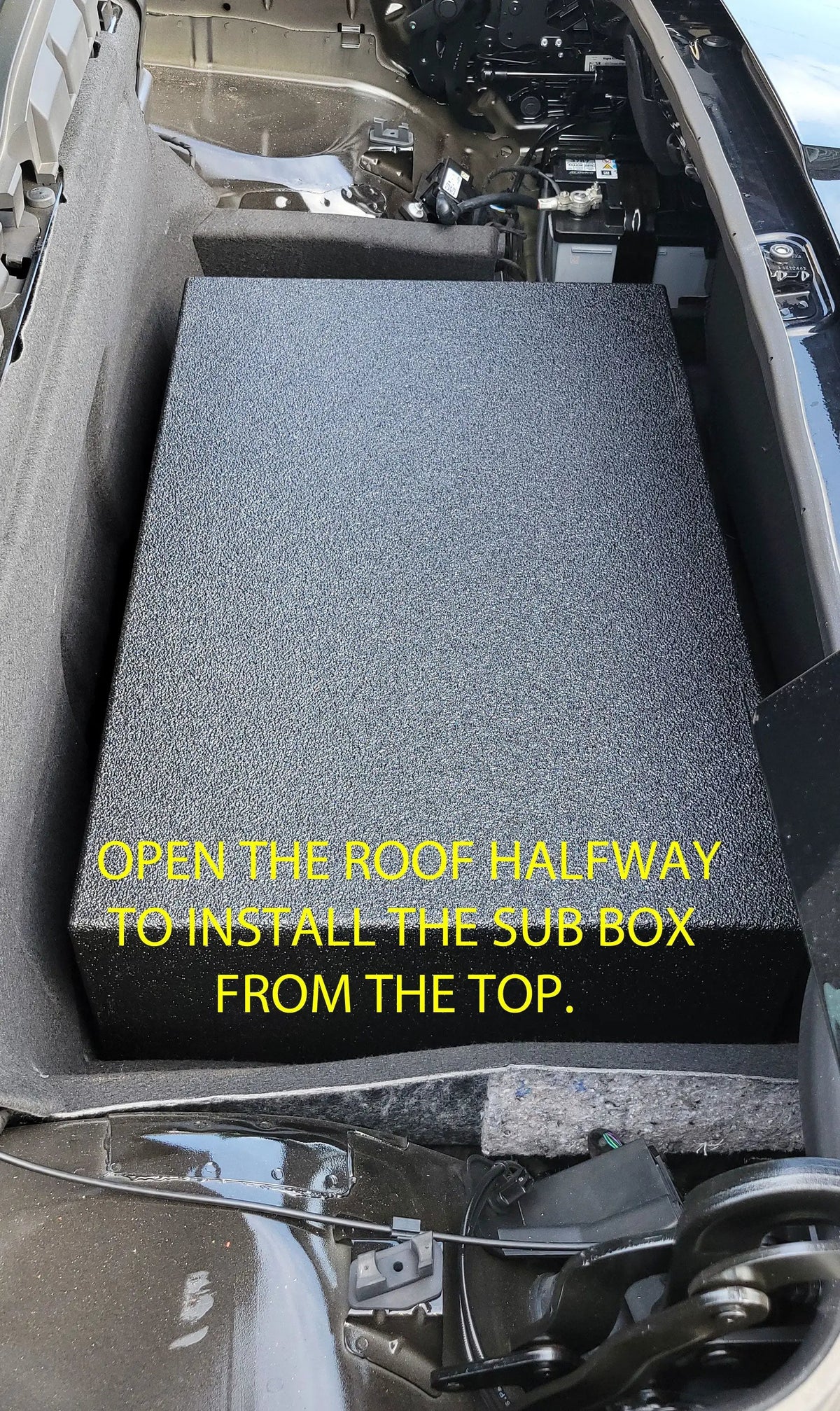 Installation photo instructing that the convertible roof be opened halfway to insert the subwoofer enclosure from above
