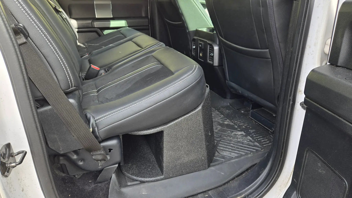 Side view of a subwoofer enclosure and its large end port beneath a rear bench seat, seen through the open rear door