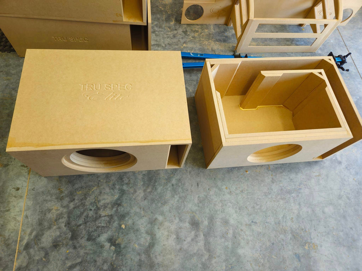 Two Tru Spec wood enclosures in a workshop, one assembled and one open to show internal bracing and the slot-port path