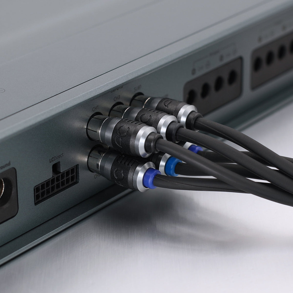 Close-up of audio or video cables plugged into the rear panel of a gray electronic device, showing black cables with silver connectors and blue ring accents.
