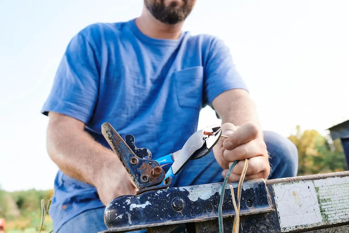 Person using blue-handled wire crimping pliers beside an outdoor metal bracket