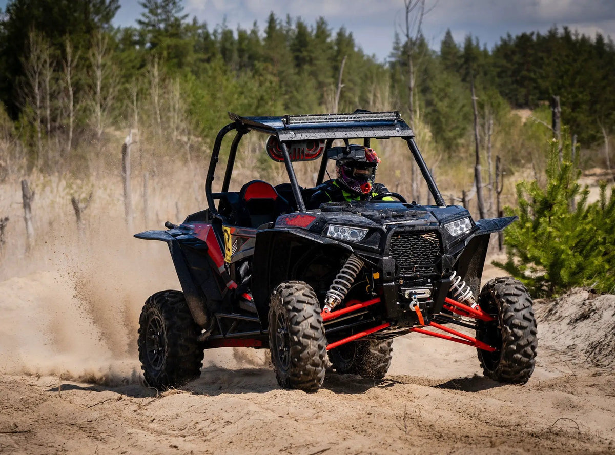A side-by-side off-road vehicle driving over a sandy trail with roof lights and red speaker grilles beneath the roof