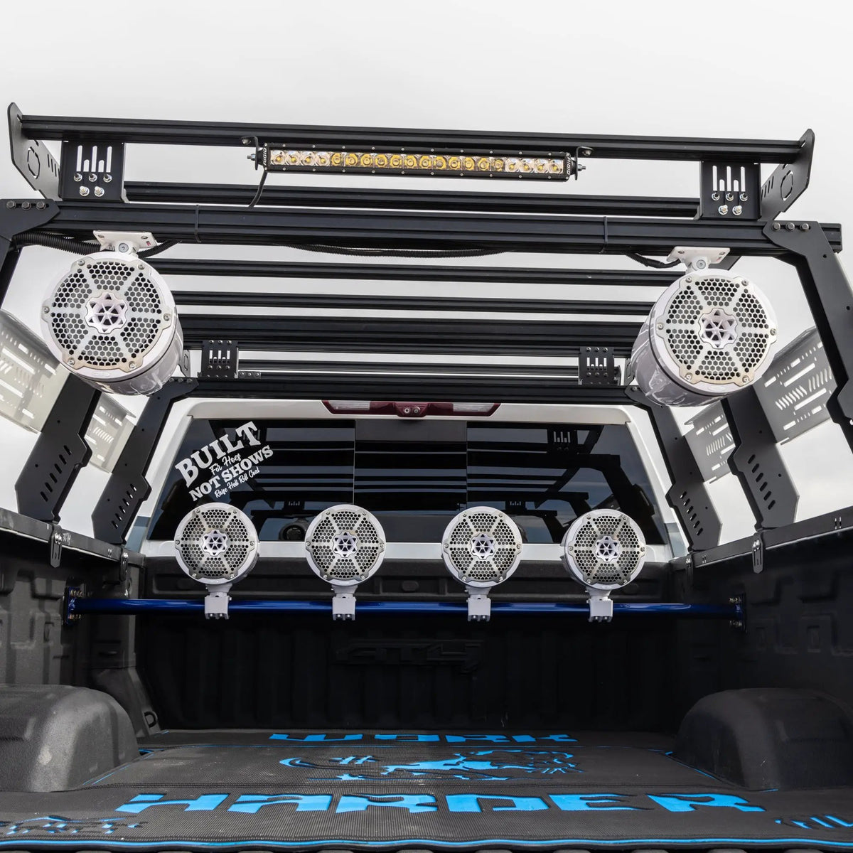 View into a vehicle's roll cage showing upper tower speakers, a light bar and a row of rear speakers