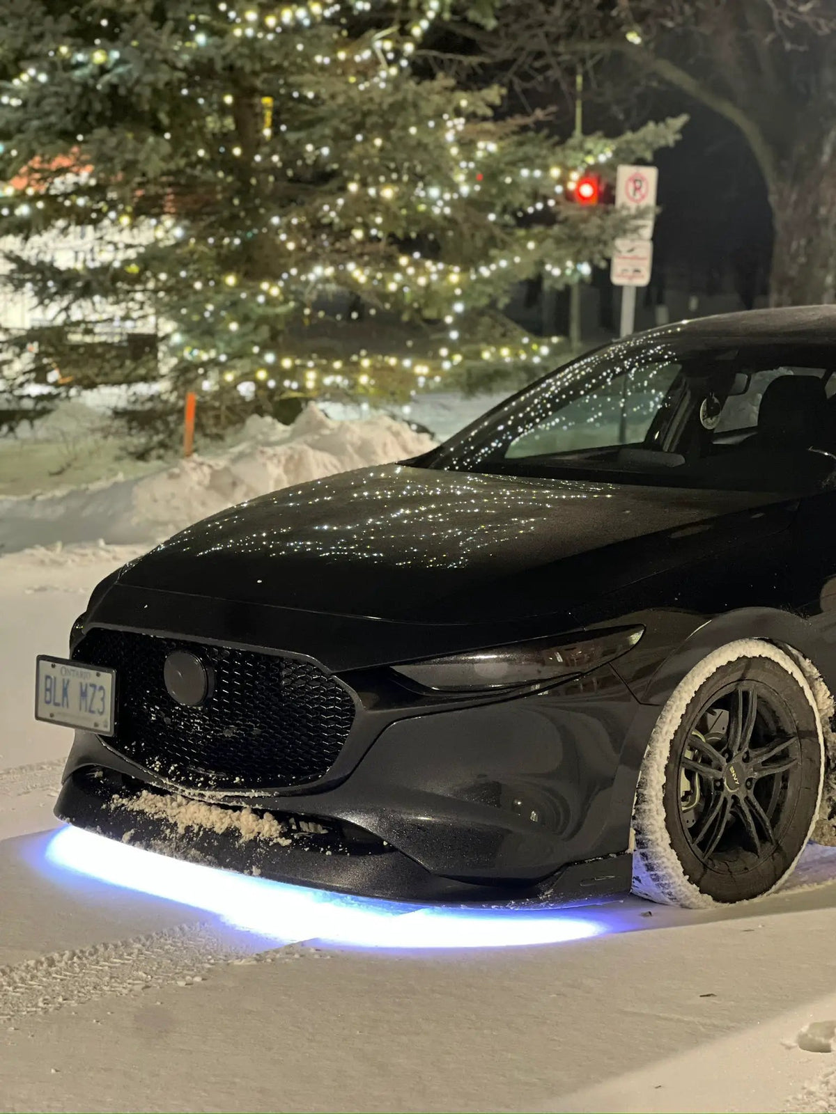 Black car in snow with blue-white underglow beneath the front bumper