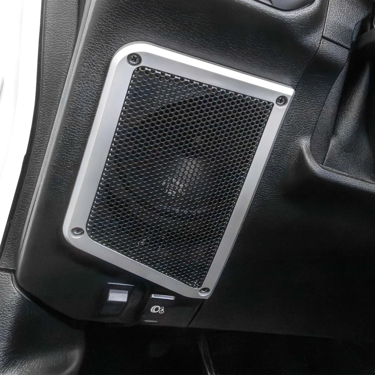 Installed subwoofer enclosure with a round mesh grille and silver mounting frame