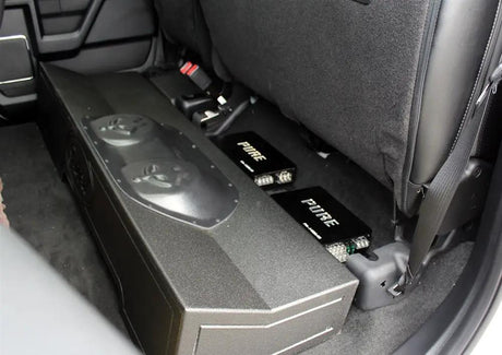 Installation example showing a subwoofer enclosure and two Pride amplifiers beneath raised rear seat cushions
