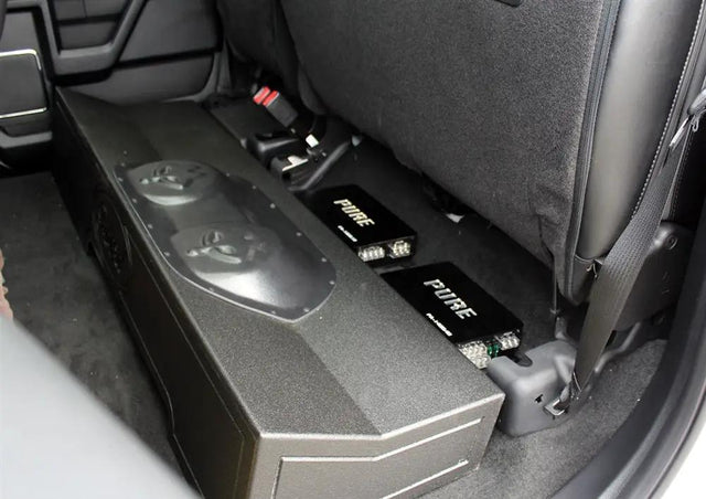 Installation example showing a subwoofer enclosure and two Pride amplifiers beneath raised rear seat cushions