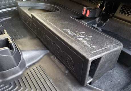 Black ported subwoofer enclosure installed beneath a raised rear seat