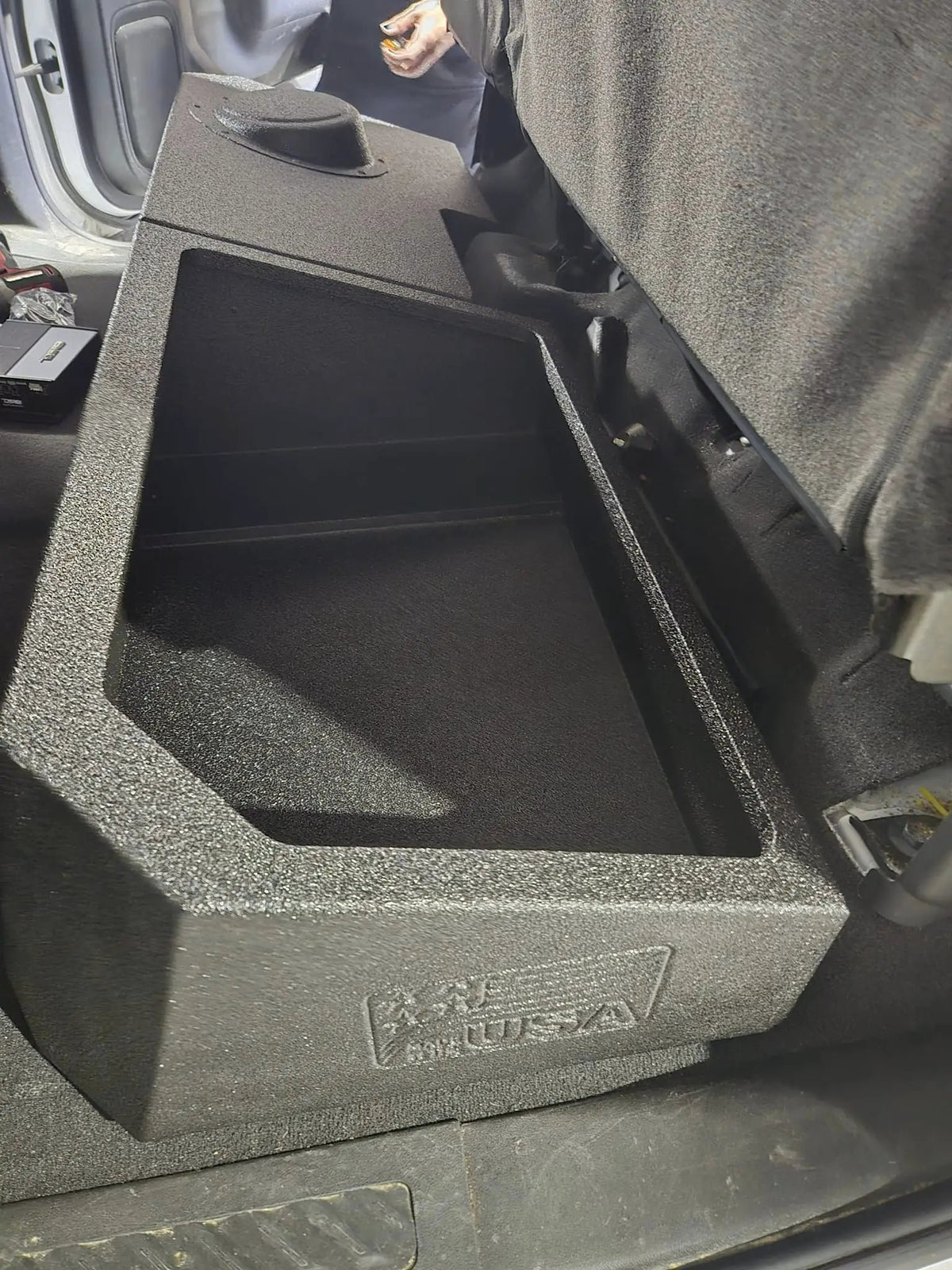 Installed FOX BOX enclosure viewed along its open storage tray beneath a raised rear seat