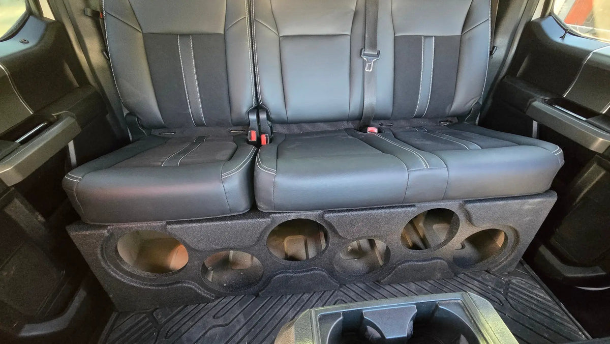 Black enclosure with six empty speaker openings installed beneath a truck rear bench seat