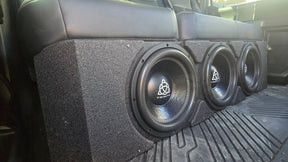 Installation example showing three Trinity subwoofers in an enclosure beneath a rear bench seat