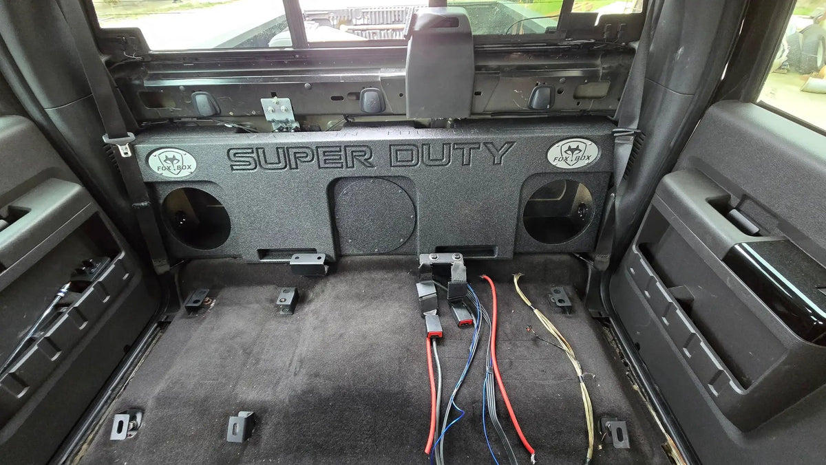 Fox Box triple-subwoofer enclosure mounted against the rear wall of a Ford Super Duty cab with the rear seat removed