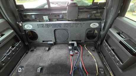Fox Box triple-subwoofer enclosure mounted against the rear wall of a Ford Super Duty cab with the rear seat removed