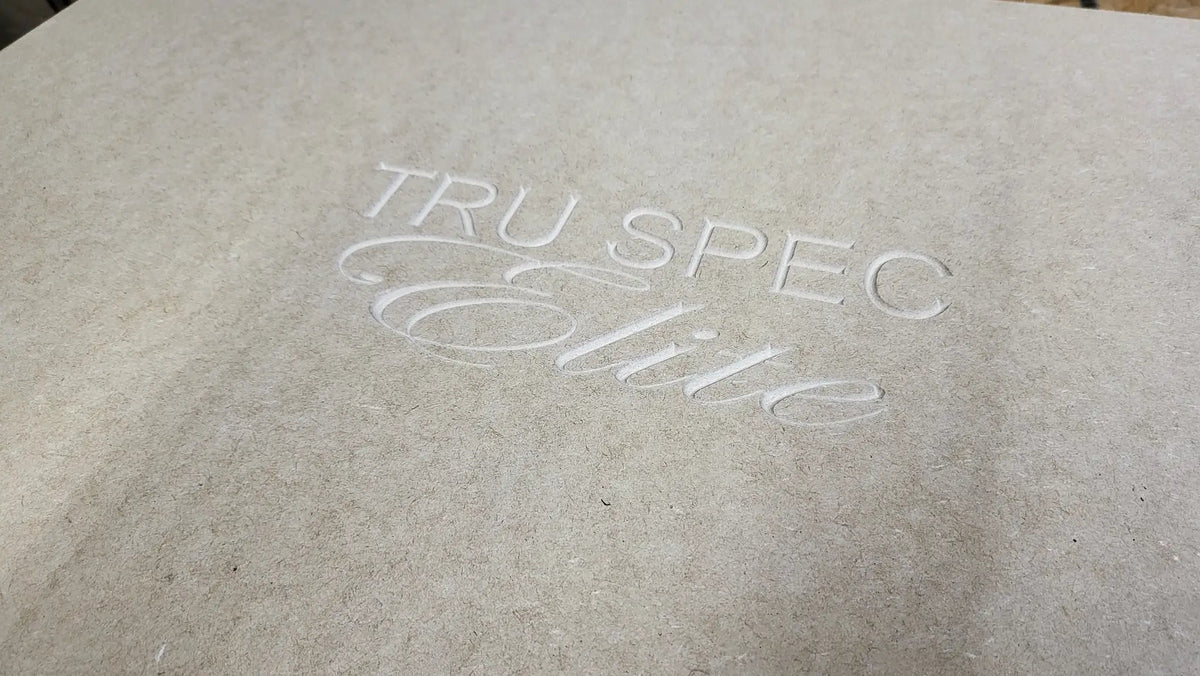 Close-up of the TRU SPEC Elite logo engraved into an unfinished wood enclosure panel