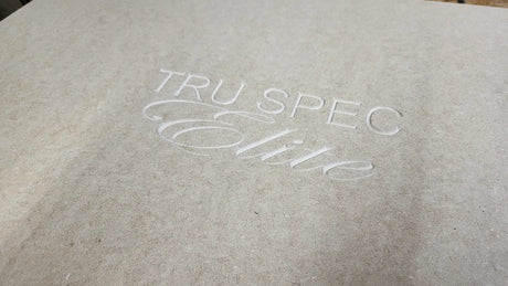 Close-up of the TRU SPEC Elite logo engraved into an unfinished wood enclosure panel
