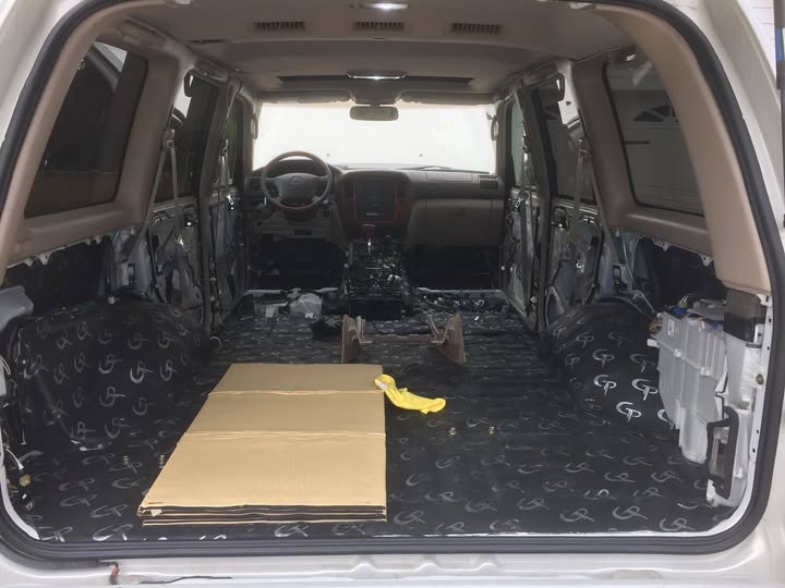 GP sound deadener covering the floor and wheel-well areas of a stripped vehicle interior, viewed from the open rear hatch