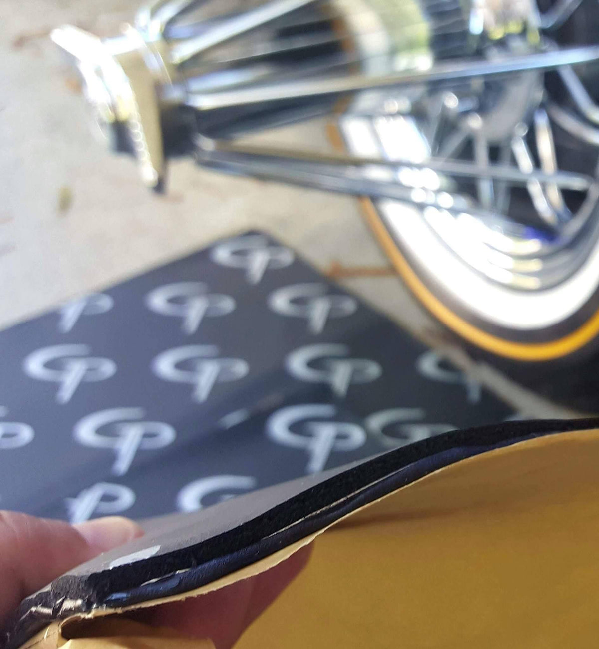 Close-up of a sound-deadening sheet bent to show its layered edge and yellow backing