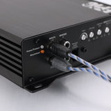 Close-up of a black audio amplifier or receiver rear panel with input jacks, control knobs, and blue-and-white cable connectors plugged in, photographed on a light gray surface.