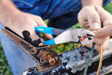 Close-up of hands crimping a red wire terminal with blue-handled pliers beside a metal bracket