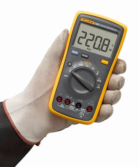 Gloved hand holding a yellow Fluke digital multimeter with a display reading 220.8