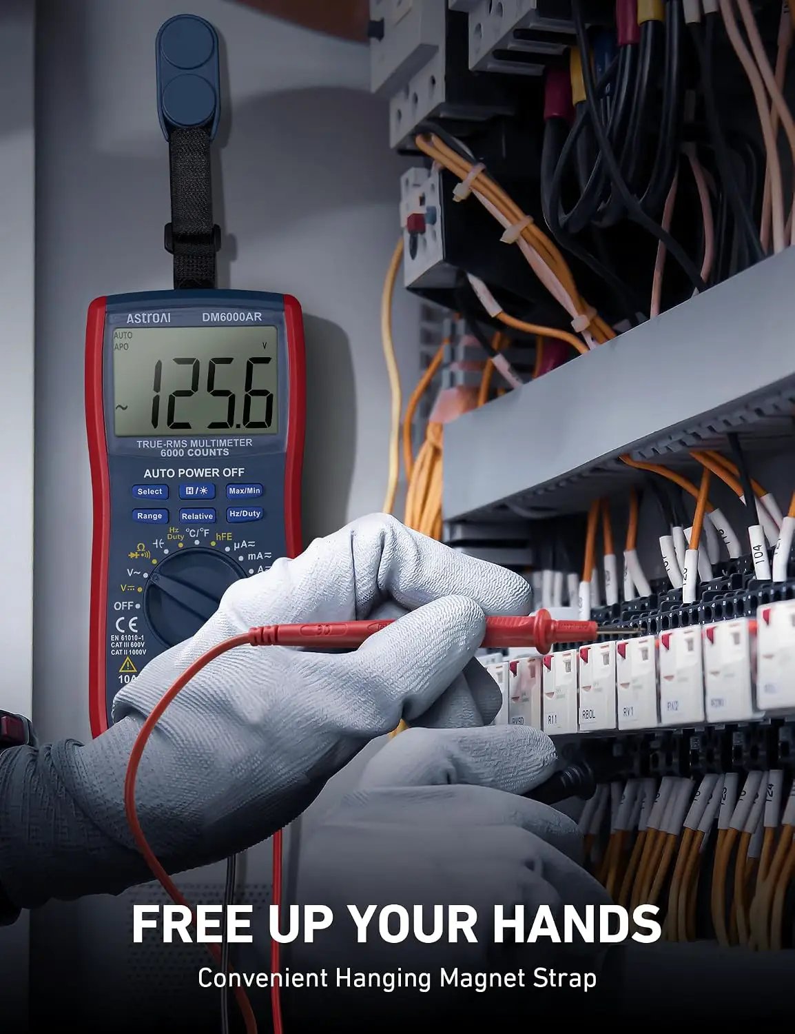 DM6000AR multimeter hanging by a magnetic strap while gloved hands use test probes at an electrical panel