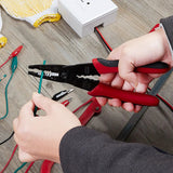 Hands using the red-and-black wire stripper on a green wire at a workbench