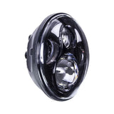 Angled view of a round black motorcycle headlight with projector lenses and partial halo