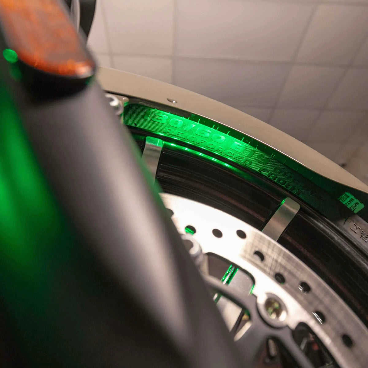 Close-up of green accent lighting illuminating a motorcycle front tire beneath the fender