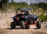 A side-by-side off-road vehicle driving over a sandy trail with roof lights and red speaker grilles beneath the roof