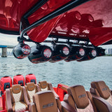 Black tower speakers mounted beneath the red canopy of a boat above rows of seats