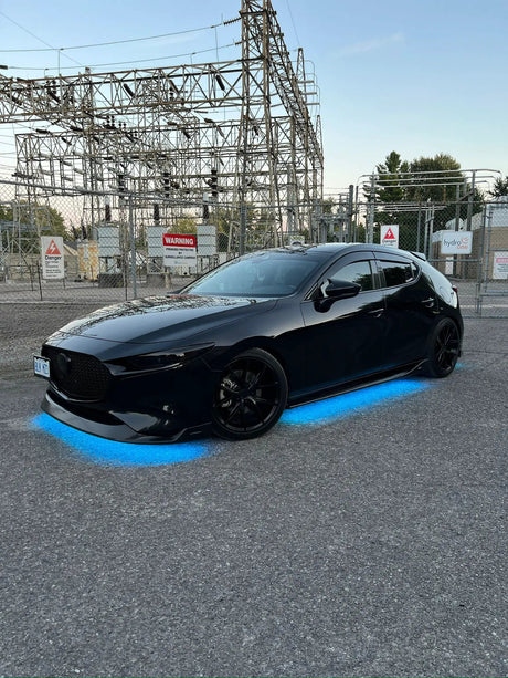 Black car with blue underbody lighting in a paved parking area