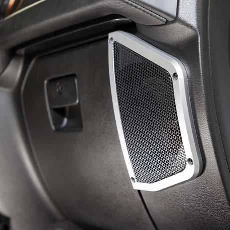 Rectangular speaker grille with silver trim installed in black vehicle interior paneling
