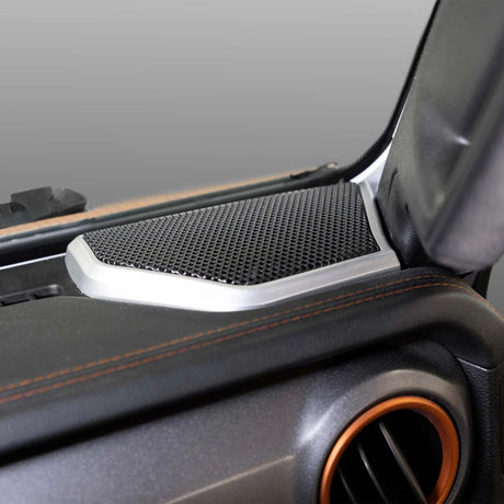 Installed dashboard-corner speaker grille with silver trim beside an orange-ringed air vent